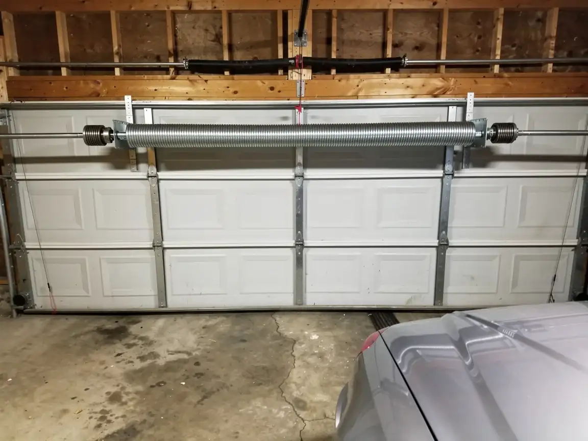 A new torsion spring is installed above a white garage door.